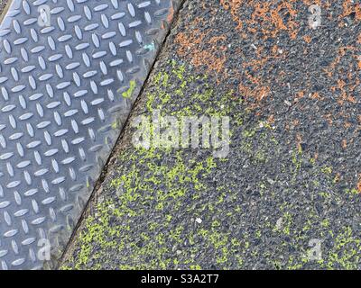 Primo piano su metallo modellato accanto all'asfalto verniciato con arancione e verde, creando uno sfondo testurizzato adatto per la composizione e la grafica Foto Stock