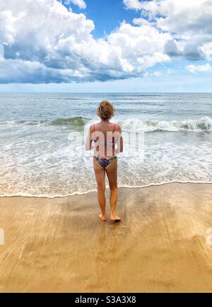 Donna in un bikini che cammina fino al bordo dell'oceano, Jacksonville Beach, Florida Foto Stock