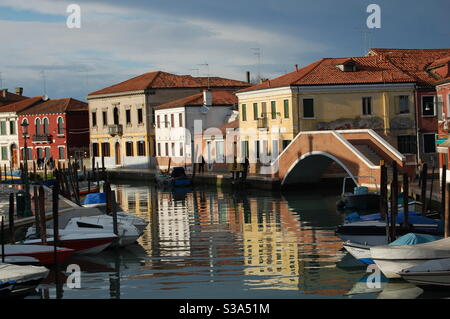 Venezia, isola di Burano, sole dopo una tempesta, facciate colorate riflettevano sul canale con il tradizionale ponte veneziano, Italia Foto Stock