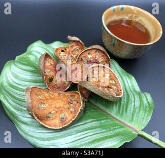 Bael essiccato (Aegle marmelos) sul lato verde del lascio con una tazza di bevanda alla frutta di bael; vista laterale; sfondo nero Foto Stock