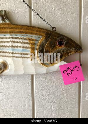 Pesce intagliato in legno su una parete di ingresso con un post si nota "Gone Fishing". Foto Stock