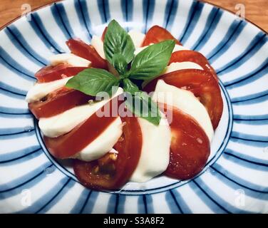Insalata caprese: Pomodoro a fette, mozzarella e foglie di basilico su un piatto blu e nero Foto Stock