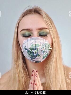 Bella giovane donna, occhi chiusi indossando maschera protettiva con mappa del mondo Foto Stock