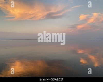 Nuvole colorate che si riflettono sulle calme acque della baia al tramonto Foto Stock