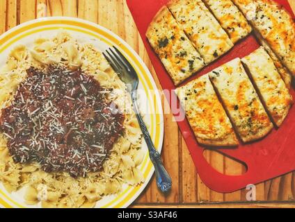 Pasta di farfalle con cravatta di fiocco con salsa di pomodoro fatta in casa, parmigiano e pane naan al formaggio all'aglio su un tavolo di legno Foto Stock