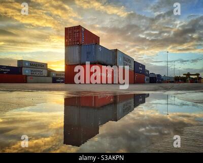 Container per l'esportazione e l'importazione impilati su un porto o una banchina al tramonto pronti per essere caricati su navi, camion e treni ferroviari Foto Stock