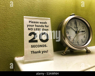 Istruzioni per lavarsi le mani durante la pandemia di Covid, e orologio per cronometrare in bagno pubblico Foto Stock