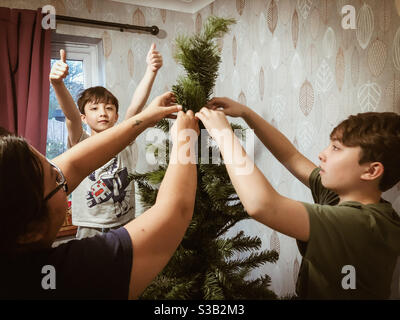 Una famiglia che passa il tempo insieme a assemblare un albero di Natale artificiale pronto per la stagione delle feste. Foto Stock