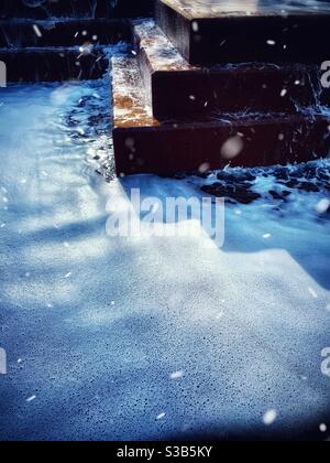 L'acqua, la neve e i gradini marroni della fontana Foto Stock