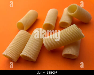 Paccheri maccheroni Pasta grezza secca italiana bronzo trafilato, Pasta di Gragnano, su sfondo arancione vista dall'alto Foto Stock