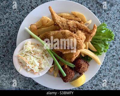 Pesce fritto, patate fritte francesi, frittelle di mais e insalata di Cole su un piatto. Foto Stock
