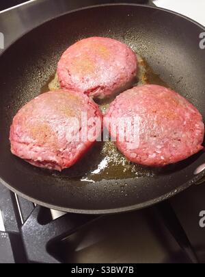 Tre polpettine di hamburger cucinando in una padella nera. Foto Stock