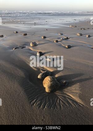 La marea in fase di receding crea modelli nella sabbia intorno ai ciottoli dentro parco statale di asilomar Foto Stock