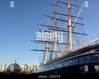 Il Cutty Sark sorge alto a Greenwich, Londra e sullo sfondo c'è Canary Wharf, che può essere raggiunto attraverso il Greenwich Foot Tunnel che conduce sotto il Tamigi. Foto Stock