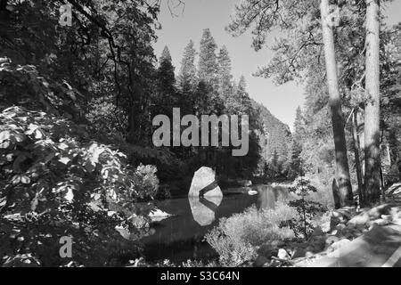 Foto drammatica in bianco e nero della valle del fiume Merced con roccia riflessa in acque ancora limpide con rive alberate del fiume, Yosemite, California Foto Stock