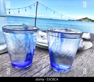 Due bicchieri blu pieni d'acqua su un tavolo con Il Mar dei Caraibi ad Antigua sullo sfondo Foto Stock