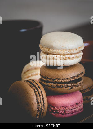 Un primo piano di deliziosi e colorati macaron con fragola al cioccolato e aroma di vaniglia e una tazza di caffè per un gustosi snack o snack Foto Stock