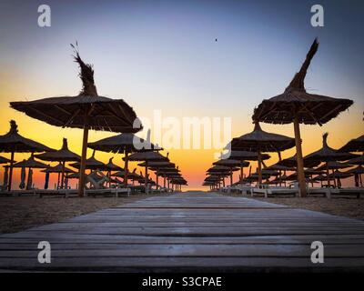 Tetti in paglia ombrelloni e lettini su una spiaggia vuota a. alba Foto Stock