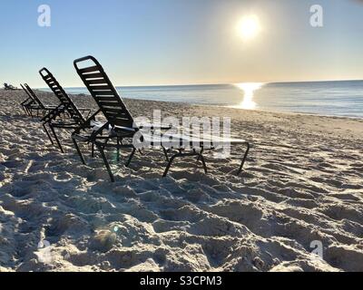 Sole sedie da spiaggia con un sole che sorge sullo sfondo, vero spiaggia Florida Foto Stock