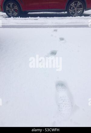 Footprint di stivale in neve fresca con auto rossa sullo sfondo, preso a Londra, Regno Unito. Foto Stock