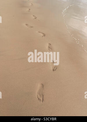 Una linea curva di impronte nella sabbia sulla spiaggia. Non camminare in linea retta Foto Stock