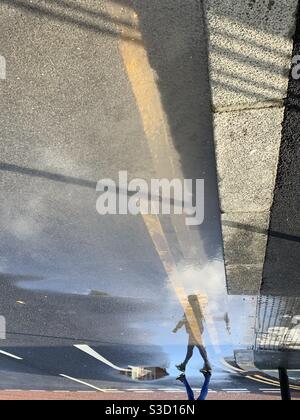 Donna che attraversa la strada in riflessione Foto Stock