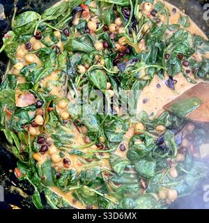 Ceci marroni e bianchi che cucinano in una pentola nera con foglie di spinaci Foto Stock