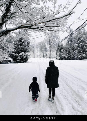 Una madre e un bambino di tre anni camminano insieme lungo una strada innevata durante una nevicata nel New Jersey. Foto Stock