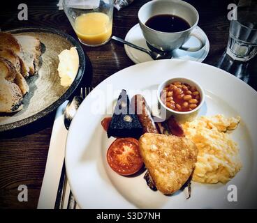 Colazione inglese completa servita su un grande piatto bianco un tavolo di legno Foto Stock