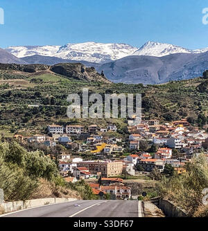 Seguire la strada fino a Beas de Granada con il Cime innevate della Sierra Nevadas Foto Stock