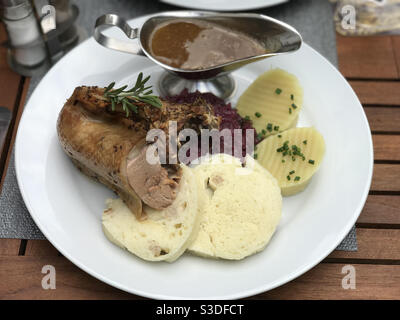 Un pasto europeo è mostrato su un piatto, composto da anatra arrosto, cavolo rosso, pane, gnocchi di patate e salsa. Foto Stock