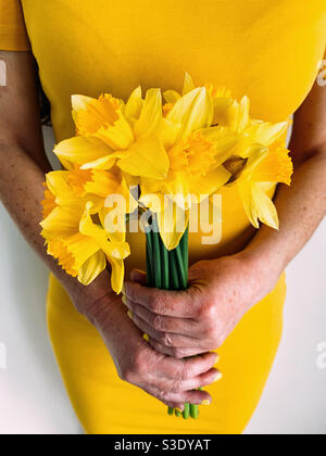 Donna che tiene un mazzo di narcisi gialli con un giallo abito Foto Stock