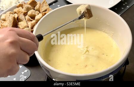 Fonduta a caquelon . La persona sta immergendo un pezzo di pane su una forchetta in formaggio fuso. Piatto tipico svizzero soprattutto in inverno. Foto Stock