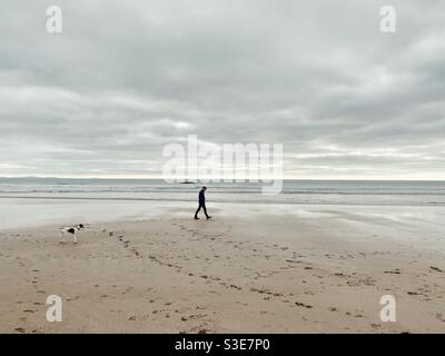 Uomo e cane camminano su una spiaggia vuota di Aberffraw nel pomeriggio di marzo, Anglesey, Galles del Nord Foto Stock