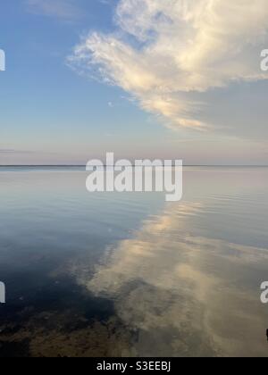 Le nuvole del tramonto che si riflettono sulle calme acque della baia Foto Stock