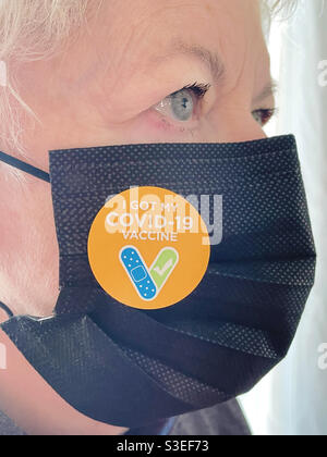 Donna anziana che indossa una maschera facciale con una prova di adesivo di vaccinazione COVID-19, USA, 2021 Foto Stock