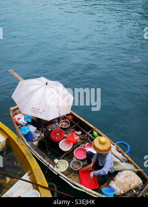 Un pescatore cinese che vende pesce e frutti di mare dalla sua barca nel porto di Aberdeen vicino AP Lei Chau a Hong Kong. Foto Stock