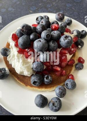 Pancake al latticello con yogurt naturale, semi di melograno e mirtilli su piatto bianco della cina Foto Stock