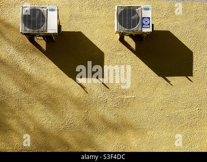 Unità di raffreddamento dei condizionatori d'aria e delle loro ombre sul parete gialla Foto Stock