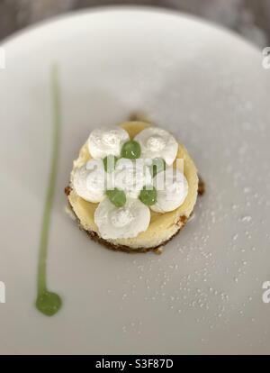 Piccola crostata di limone ricostruita su crumble coperto con chantilly fatto in casa panna montata e coulis di lime su un piatto da ristorante bianco Foto Stock