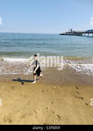 Ragazzo che gioca sulla spiaggia con molo Foto Stock
