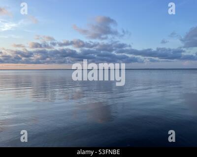 Il cielo morbido del tramonto si riflette sulle calme acque della baia Foto Stock