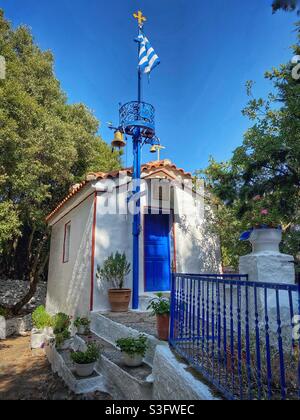 Piccola chiesa greca con bandiera greca a nord dell'isola di Skiathos. Foto Stock