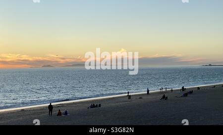 Gente silhoueted sulla spiaggia a Point Mugu, California, con il sole che tramonta sull'Oceano Pacifico. Isola di Catalina visibile all'orizzonte Foto Stock