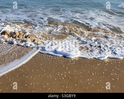 Acqua di mare schiumosa che lambe una spiaggia di sabbia Foto Stock