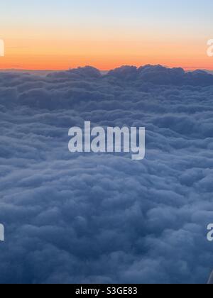 Tramonto visto da un aereo con nuvole che si stagliano davanti e un cielo arancione in lontananza. Foto Stock