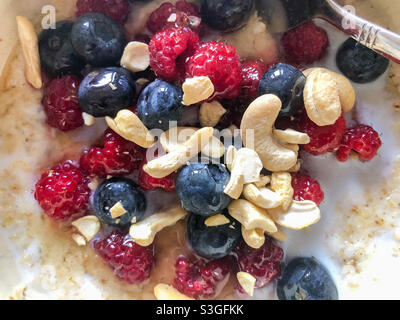 Primo piano vista del porridge con lamponi, mirtilli e noci di anacardi per colazione. Foto Stock