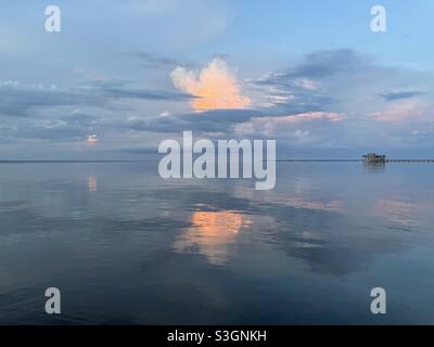 Nuvole colorate al tramonto che si riflettono sulle calme acque della baia Foto Stock
