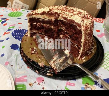 Tagliare la torta di velluto rosso con la taglierina per torte e le briciole sparse su un panno di plastica da tavola per compleanno Foto Stock