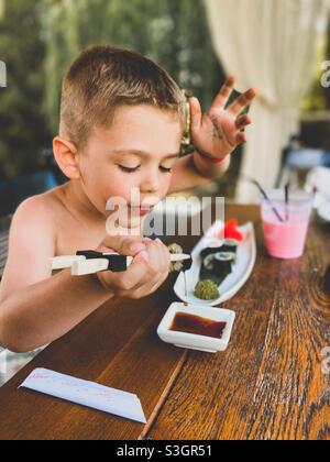 Ragazzo di cinque anni che mangia sushi e beve una frullato all'aperto Foto Stock